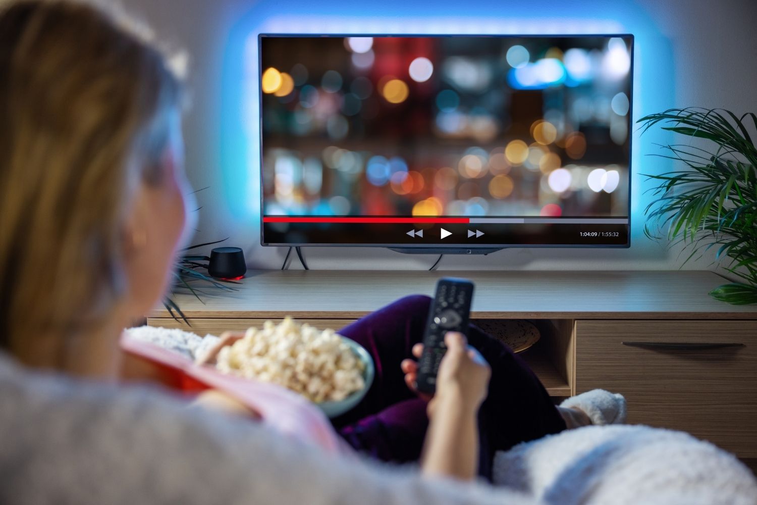 E Frau hocket am Abig dehai und gnüsst die scharf Bildqualität vo ere IPTV Box uf eme grosse Smart TV mit Hintergrundbelüchtig.