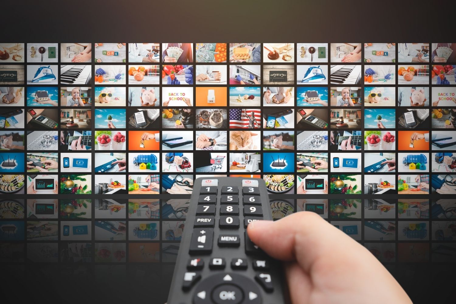 E Hand bedient d’Fernbedienig vor ere Wand mit vielne Film-Vorschau-Bilder vom IPTV Player für e grossi Uswahl.